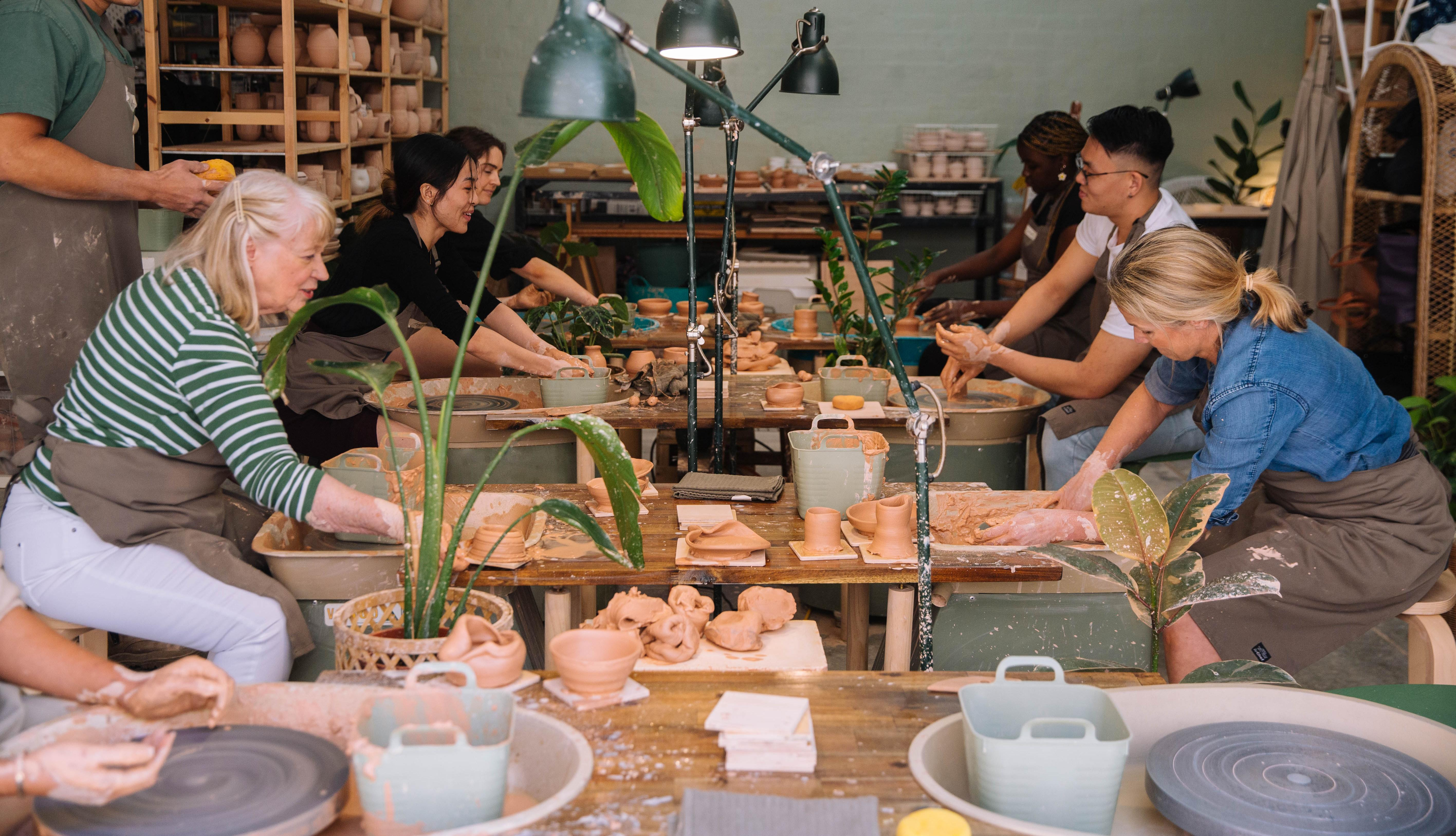 Group of people sitting behind pottery wheels